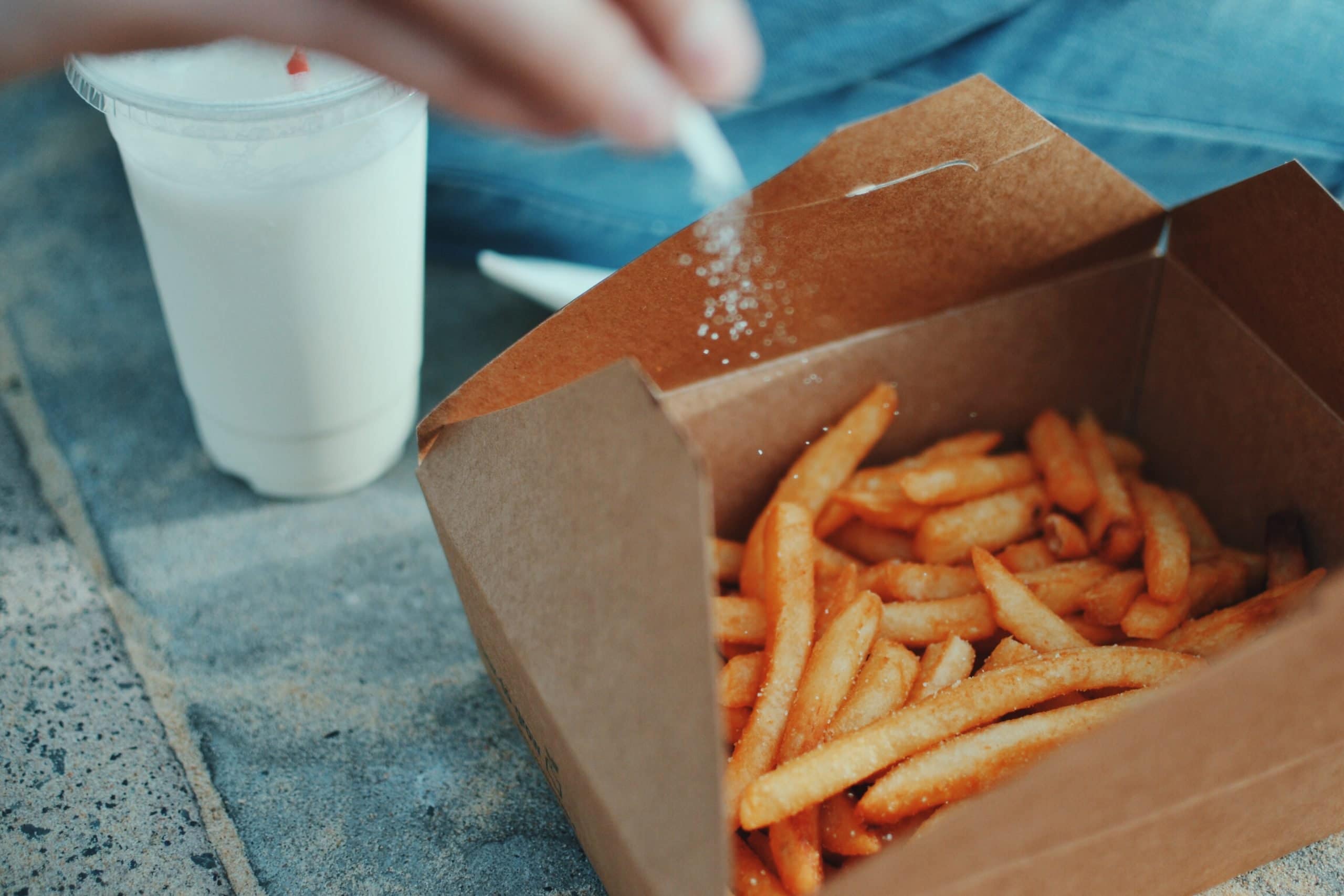 Chips in a brown box with a hand adding salt