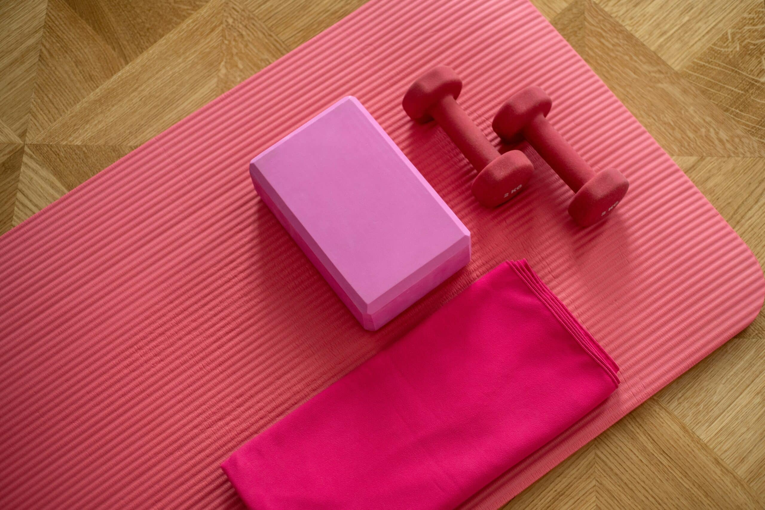 Pink yoga mat with a pink yoga block and two pink weights